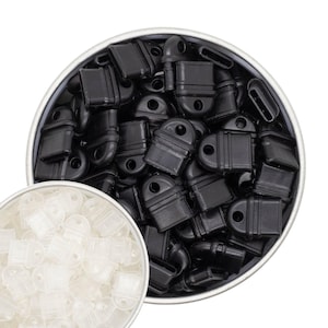 May include: A metal tin filled with numerous black plastic cord locks, each with a rectangular body and a circular hole. A smaller container holds a collection of translucent white cord locks.