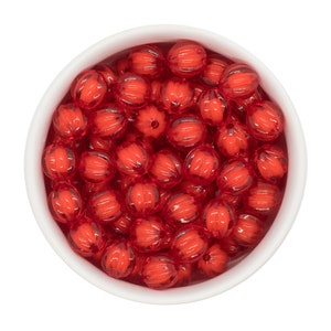 May include: A bowl filled with red, translucent, faceted beads. The beads have a ribbed texture and are arranged in a random pattern.