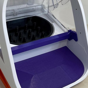 Puede incluir: Caja de arena para gatos automática de limpieza automática blanca con una tapa de plástico transparente y una bandeja de arena morada. La tapa tiene una pegatina que dice "#1 Cat Leo".