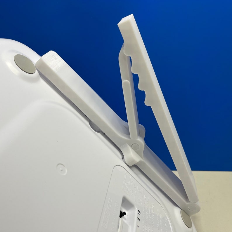 Puede incluir: B&aacute;scula digital blanca con un asa de pl&aacute;stico blanco que se pliega. El asa tiene una serie de crestas en el lateral.