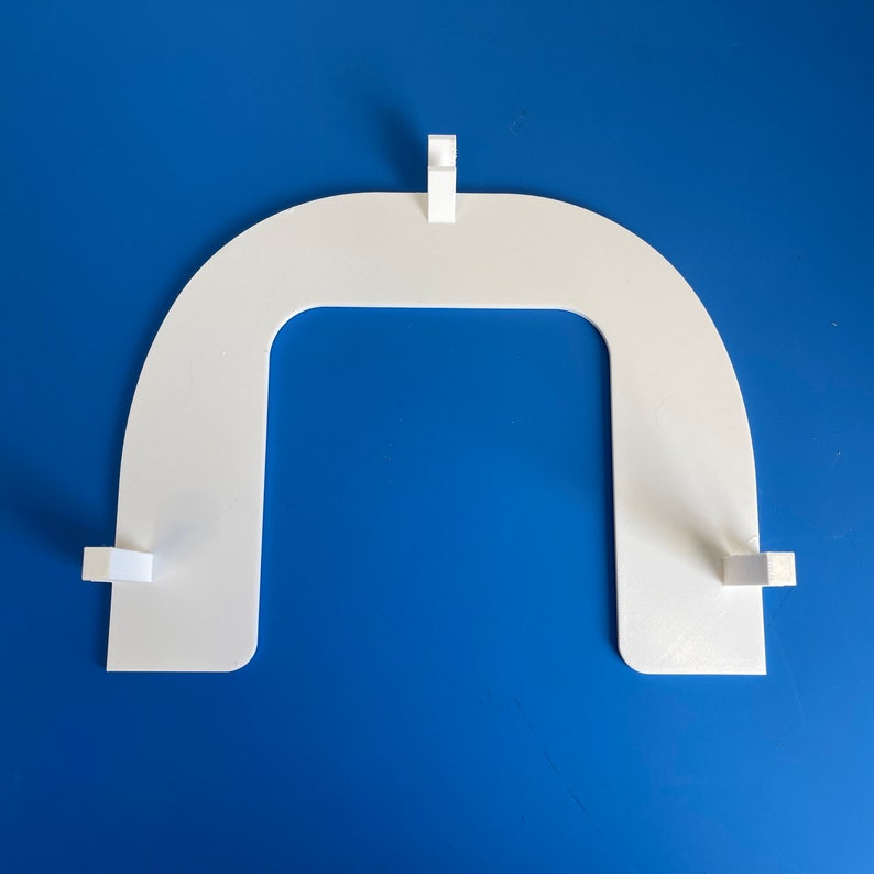 May include: White plastic frame with a rounded top and a rectangular opening in the center. The frame has four small tabs on the sides.