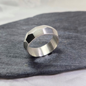 May include: A silver ring with a faceted, geometric design. The ring is made of polished metal and has a smooth, rounded interior.