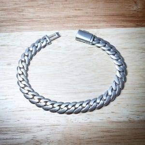 May include: A silver curb chain bracelet with a clasp fastening. The bracelet is made of a thick, chunky chain.