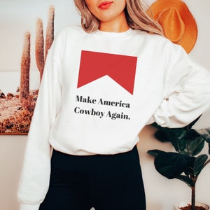 Puede incluir: Sudadera blanca con un gr&aacute;fico rojo de un cigarrillo y el texto "Make America Cowboy Again."