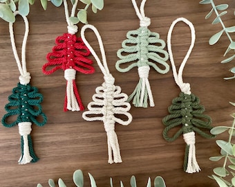 May include: Five handmade macrame Christmas tree ornaments in red, green, and natural colors. The ornaments are made with cotton cord and have a tassel at the bottom.