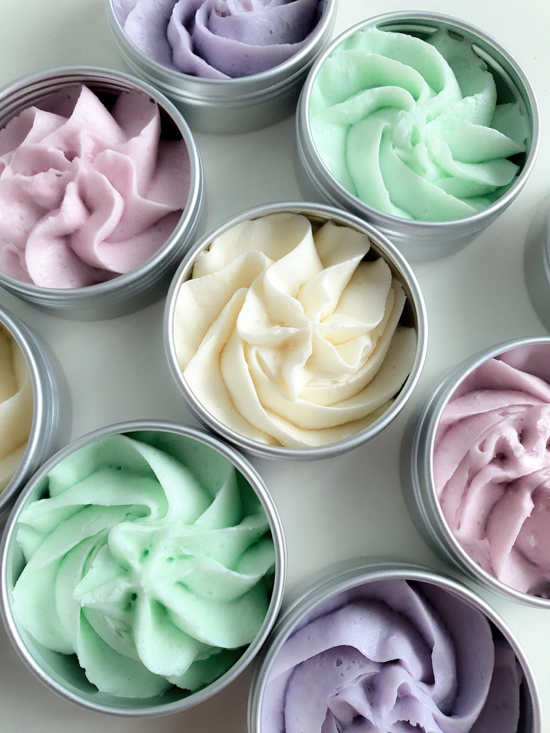 Puede incluir: Seis peque&ntilde;as latas plateadas llenas de cremas batidas de diferentes colores. Las cremas est&aacute;n en espiral y tienen una textura suave y cremosa. Los colores son lavanda, verde claro, blanco y un tono de lavanda m&aacute;s oscuro.