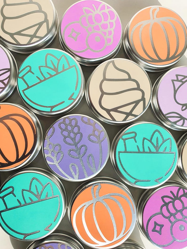 Puede incluir: Una colecci&oacute;n de 10 peque&ntilde;as latas redondas de plata con varios dise&ntilde;os coloridos. Los dise&ntilde;os incluyen una calabaza, un cono de helado, un taz&oacute;n de plantas, un racimo de bayas y flores de lavanda.