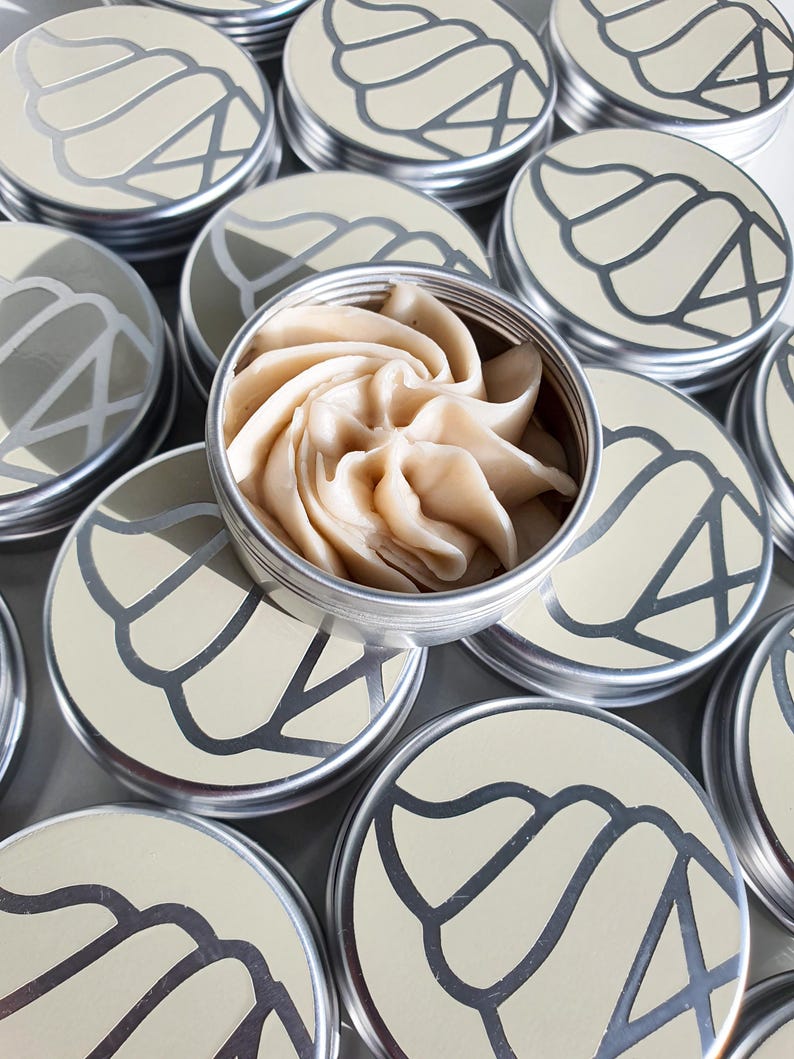 May include: Several silver tins with a swirl design on the lid. The tins are filled with a beige, whipped cream-like substance.