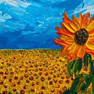 May include: A vibrant orange sunflower with a dark brown centre stands out against a field of yellow sunflowers. The sky is a bright blue with white clouds.