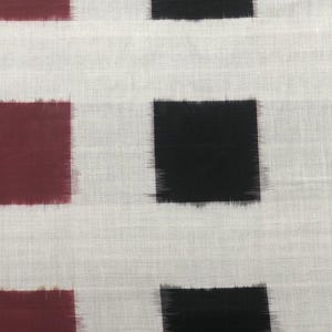 May include: Close-up of a fabric with a repeating pattern of maroon and black squares on a white background. The squares have a slightly blurred, brushstroke-like appearance, creating a textured effect. The fabric appears to be cotton or linen.
