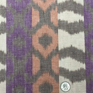 May include: Close-up of a fabric with a repeating pattern of purple, orange, and brown ikat stripes. A US quarter is included for scale.