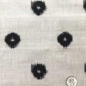 May include: White fabric with a black ikat pattern. The pattern is a series of small, black circles with a white center. The fabric is textured and has a subtle sheen.