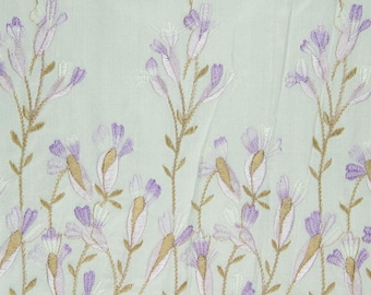May include: Pale blue fabric with embroidered floral design. The flowers are in shades of purple, pink, and white with brown stems.