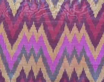 May include: Close-up of a textile with a vibrant zigzag pattern. The design features alternating bands of colors including pink, gold, burgundy, and gray. The fabric has a slightly textured appearance, suggesting a woven material.