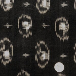 May include: Black fabric with a white ikat pattern. The pattern is a repeating geometric design of squares and rectangles.