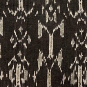 May include: Black fabric with a white ikat pattern. The fabric has a woven texture and a subtle sheen.