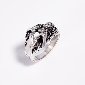 May include: A silver-toned metal ring featuring a sculpted, three-dimensional design of a reclining figure with long, flowing hair. The surface has an oxidized finish with dark recessed areas that highlight the intricate details of the form.
