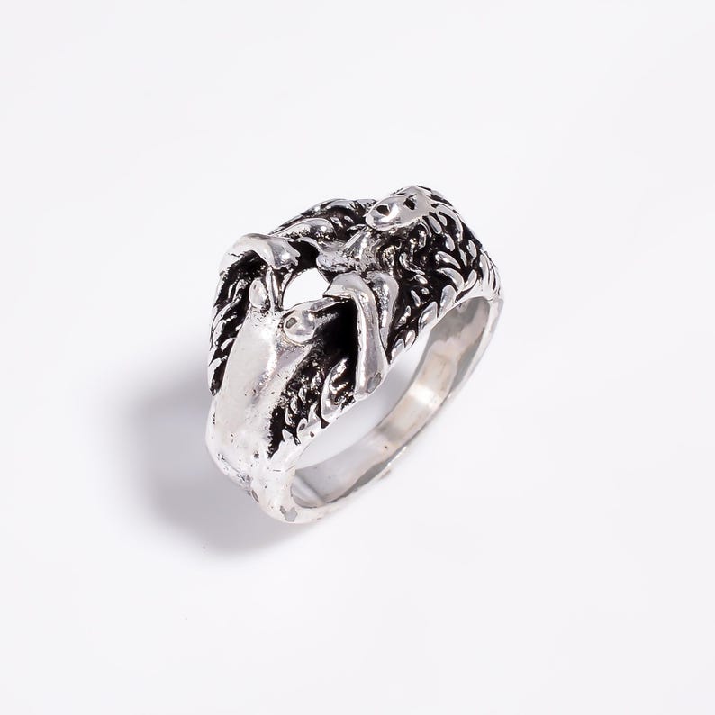 May include: A silver-toned metal ring featuring a sculpted, three-dimensional design of a reclining figure with long, flowing hair. The surface has an oxidized finish with dark recessed areas that highlight the intricate details of the form.