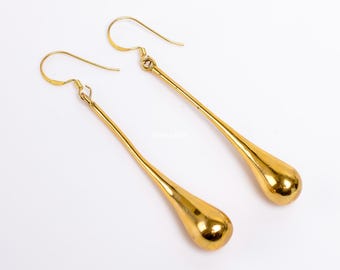 Puede incluir: Un par de aretes largos de gota de oro con forma de lágrima. Los aretes están hechos de metal y tienen un acabado brillante.
