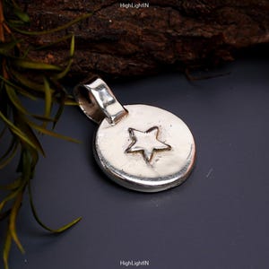 May include: A silver pendant with a star design. The pendant is round and has a loop at the top for attaching to a chain.