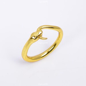 May include: A gold snake ring featuring a detailed snake head design. The ring is made of metal and has a smooth finish.