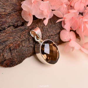 May include: A silver pendant with a brown oval gemstone. The gemstone is faceted and has a shiny finish.
