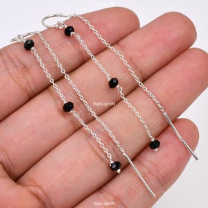 May include: A pair of silver dangle earrings with black beads and a long chain. The earrings are about 2 inches long.