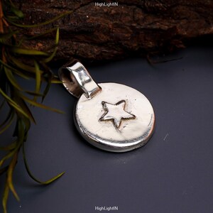 May include: A silver pendant with a star design. The pendant is round and has a loop at the top for attaching to a chain.