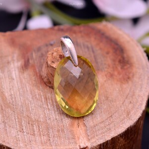May include: A yellow faceted gemstone pendant with a silver bail. The pendant is oval shaped and has a light yellow color.