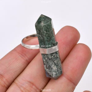 Può includere: Un anello d'argento con una punta di cristallo verde e grigia. Il cristallo è a punta e incastonato in una fascia d'argento.