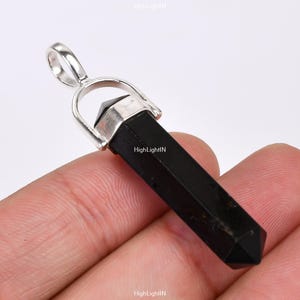 May include: Black obsidian crystal point pendant with a silver bail. The pendant is approximately 2 inches long.