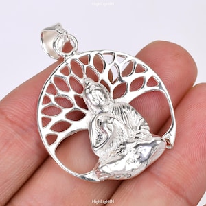 Puede incluir: Pendiente de plata con una representación detallada de una figura de Buda meditando dentro de un diseño de árbol de la vida. El pendiente es circular y tiene un diseño delicado e intrincado.