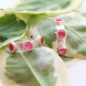 Può includere: Un paio di orecchini a cerchio d'argento con tre pietre preziose rosa incastonate in ogni cerchio.