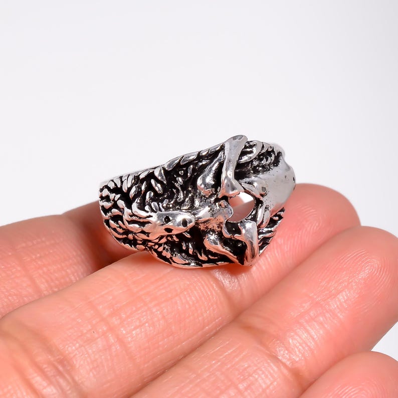 May include: A silver-toned metal ring featuring a textured, oxidized finish with a complex, raised design that resembles intertwined organic shapes or bone-like structures, creating a rugged, high-contrast appearance across the entire band.