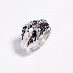May include: A silver-toned metal ring featuring a sculpted, three-dimensional design of a reclining figure with long, flowing hair. The surface has an oxidized finish with dark recessed areas that highlight the intricate details of the form.