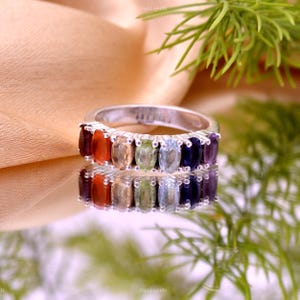 May include: A silver ring with a row of oval-shaped gemstones in shades of red, orange, yellow, green, blue, and purple.