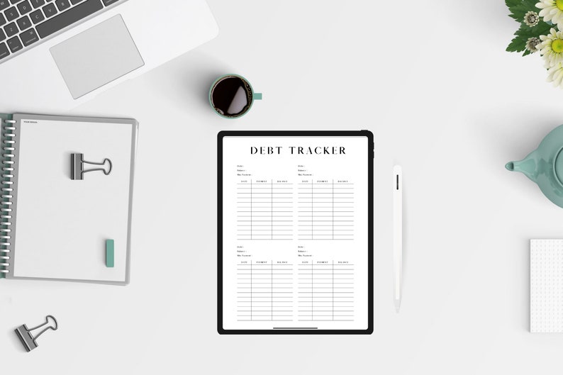 May include: A white tablet with a black border displaying a debt tracker spreadsheet. The tablet is on a white surface with a cup of coffee, a notebook, a pen, and a teapot.