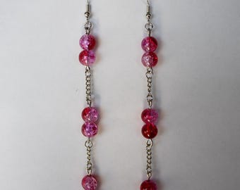 May include: A pair of dangle earrings featuring a chain of silver links and multiple red and pink crackle glass beads. The earrings have a fish hook closure.