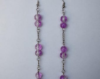 May include: A pair of long, silver chain earrings with purple and clear glass beads. The beads are round and have a speckled texture.