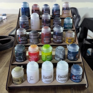 May include: A wooden paint rack with multiple rows of small paint bottles. The bottles are labelled "Citadel Colour" and have various colours, including red, green, blue, and black.