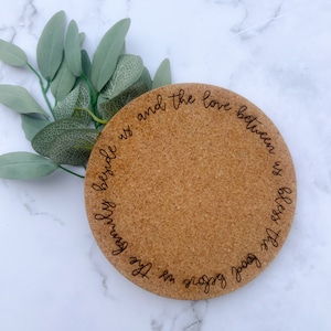 May include: A round cork coaster with the text "Food before us, the family beside us and the love between us bless the" engraved on it.