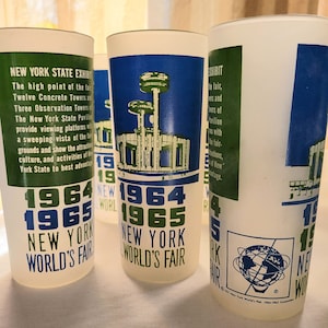 May include: Three blue and white plastic cups with the text "1964 1965 New York World's Fair" printed on them. The cups have a green and white design with a globe graphic on one cup.