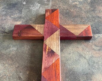 May include: A wooden cross made of different types of wood, with a geometric pattern of triangles. The wood is a mix of reddish-brown, purple, and light brown.