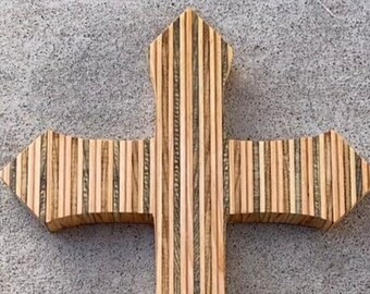 May include: A wooden cross made of plywood with a striped pattern. The cross is a light brown color with darker brown stripes.