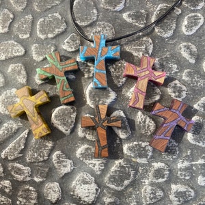 May include: A necklace with six wooden cross pendants. The crosses are all different colors and have a stained glass look. The necklace is made of black cord.