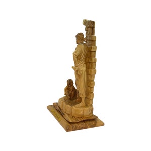 May include: A hand-carved wooden sculpture of Saint Joseph standing next to a wall with a dog at his feet. The sculpture is made of olive wood and is mounted on a wooden base. The base has the words "St. Joseph" inscribed on it.