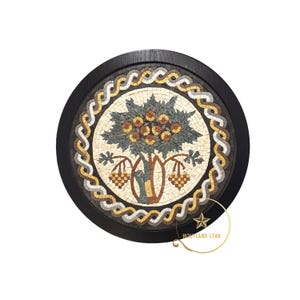 May include: Round mosaic art piece featuring a tree with fruit and leaves, surrounded by a decorative border. The mosaic is set within a black wooden frame. The tree design includes shades of green, brown, and gold, creating a detailed and artistic appearance.
