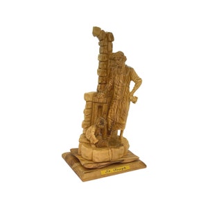May include: Hand-carved wooden figurine of Saint Joseph, depicted as a carpenter, standing next to a small child. The figurine is made of olive wood and has a natural wood finish. The base of the figurine is inscribed with the words "St. Joseph".