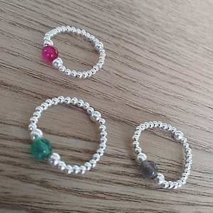 May include: Three silver beaded rings with a single gemstone bead. The rings feature a pink, green, and grey gemstone.