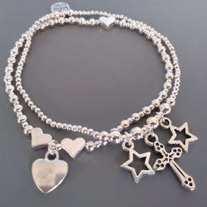 May include: A silver bracelet with multiple charms, including hearts and stars. The bracelet is made of small silver beads and has a charm with a cross.